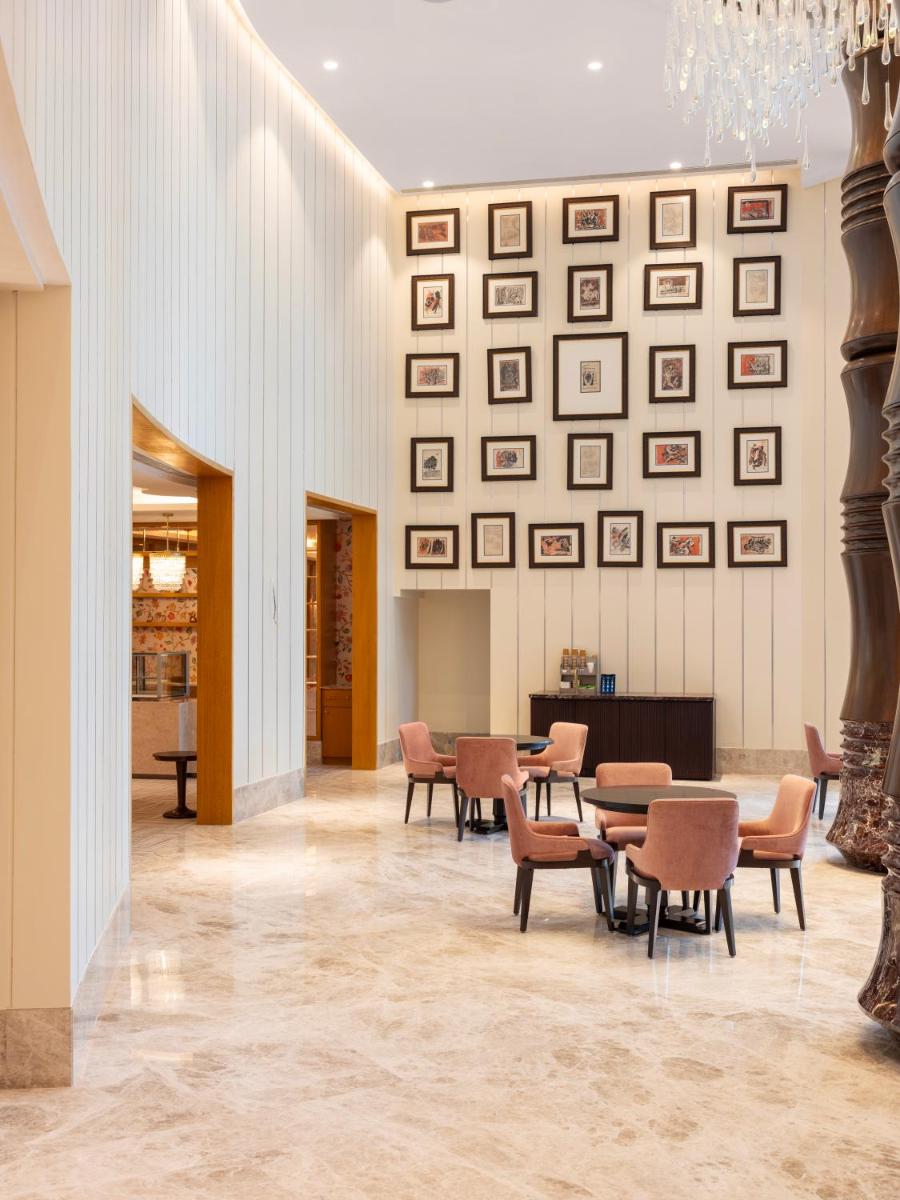 a lobby with tables and chairs and pictures on the wall at The Leela Hyderabad Banjara Hills in Hyderabad
