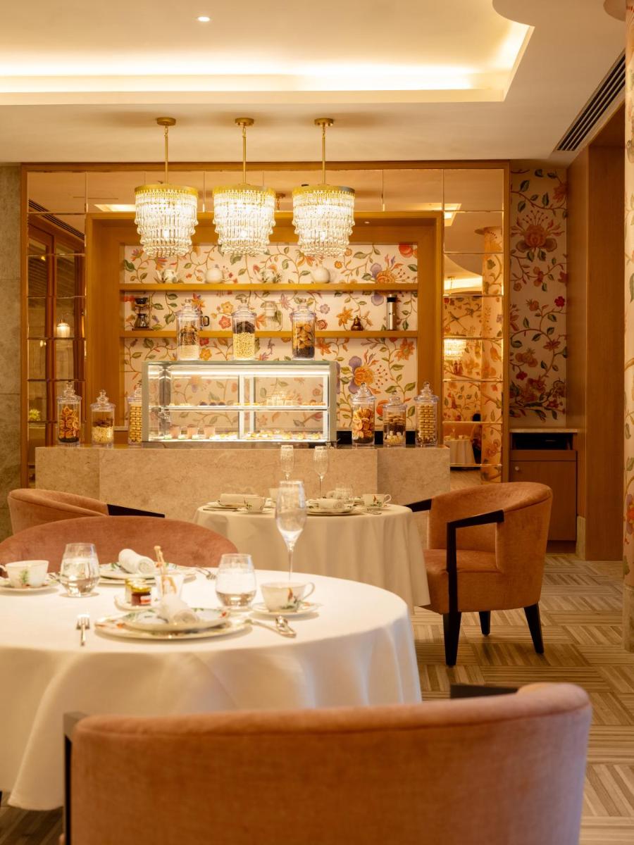 a restaurant with white tables and chairs and chandeliers at The Leela Hyderabad Banjara Hills in Hyderabad