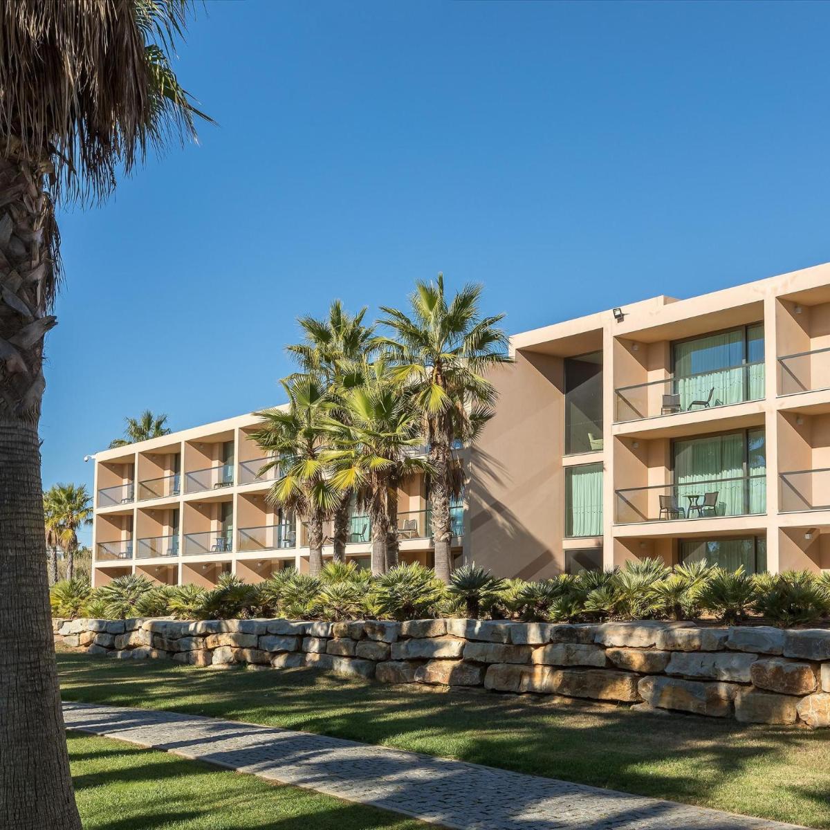 um edifício de apartamentos com palmeiras e uma parede de retenção em Kimpton Atlantico Algarve by IHG em Albufeira