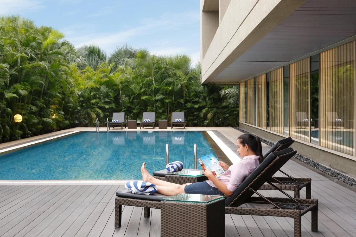 a woman sitting in a chair next to a swimming pool at Courtyard by Marriott Pune Hinjewadi in Pune