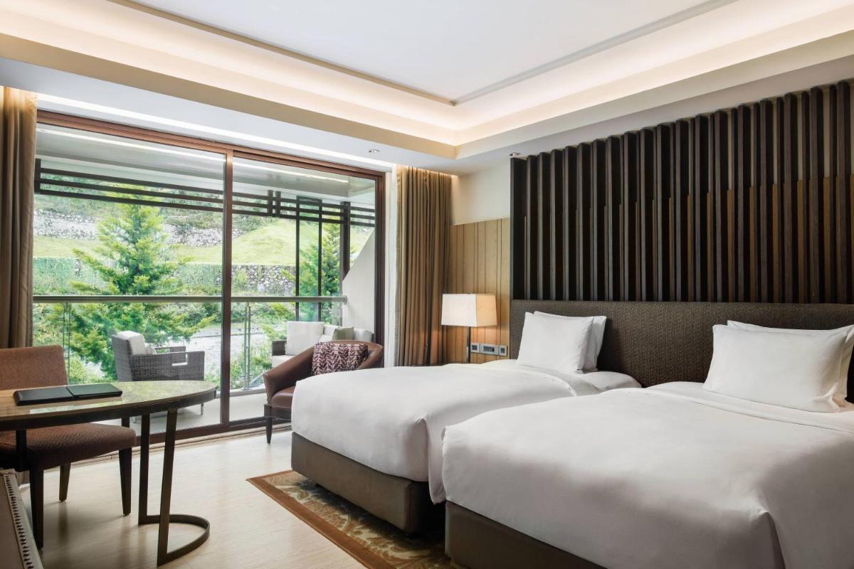 a hotel room with two beds and a large window at JW Marriott Mussoorie Walnut Grove Resort & Spa in Mussoorie