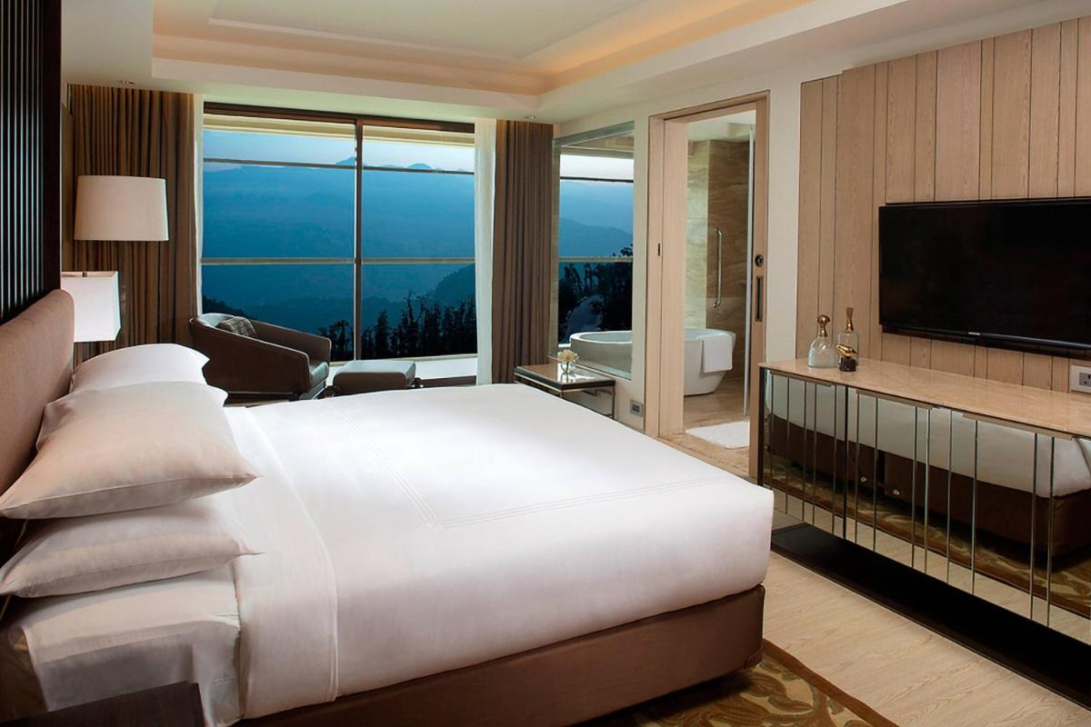 a bedroom with a large white bed and a television at JW Marriott Mussoorie Walnut Grove Resort & Spa in Mussoorie