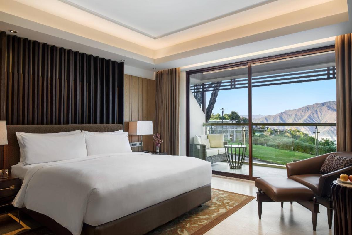 a bedroom with a large bed and a large window at JW Marriott Mussoorie Walnut Grove Resort & Spa in Mussoorie