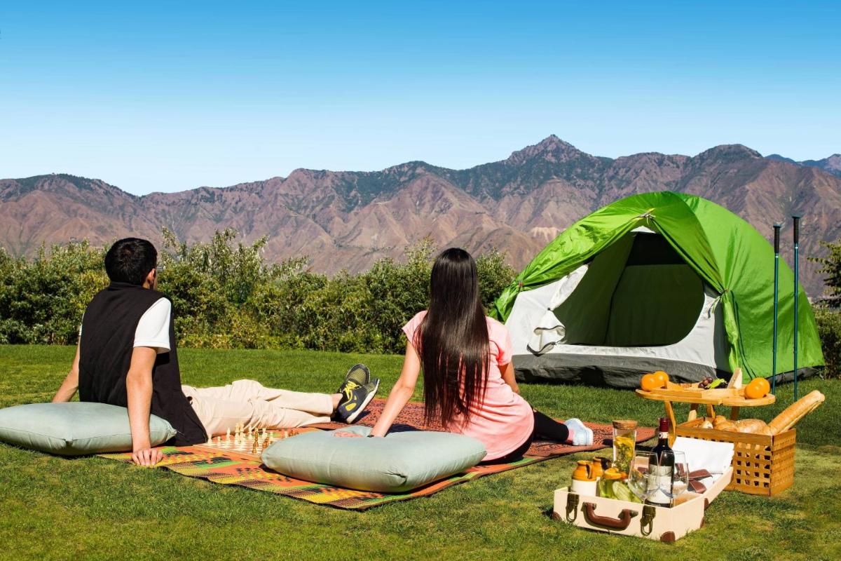 a man and woman sitting on a blanket in front of a tent at JW Marriott Mussoorie Walnut Grove Resort & Spa in Mussoorie