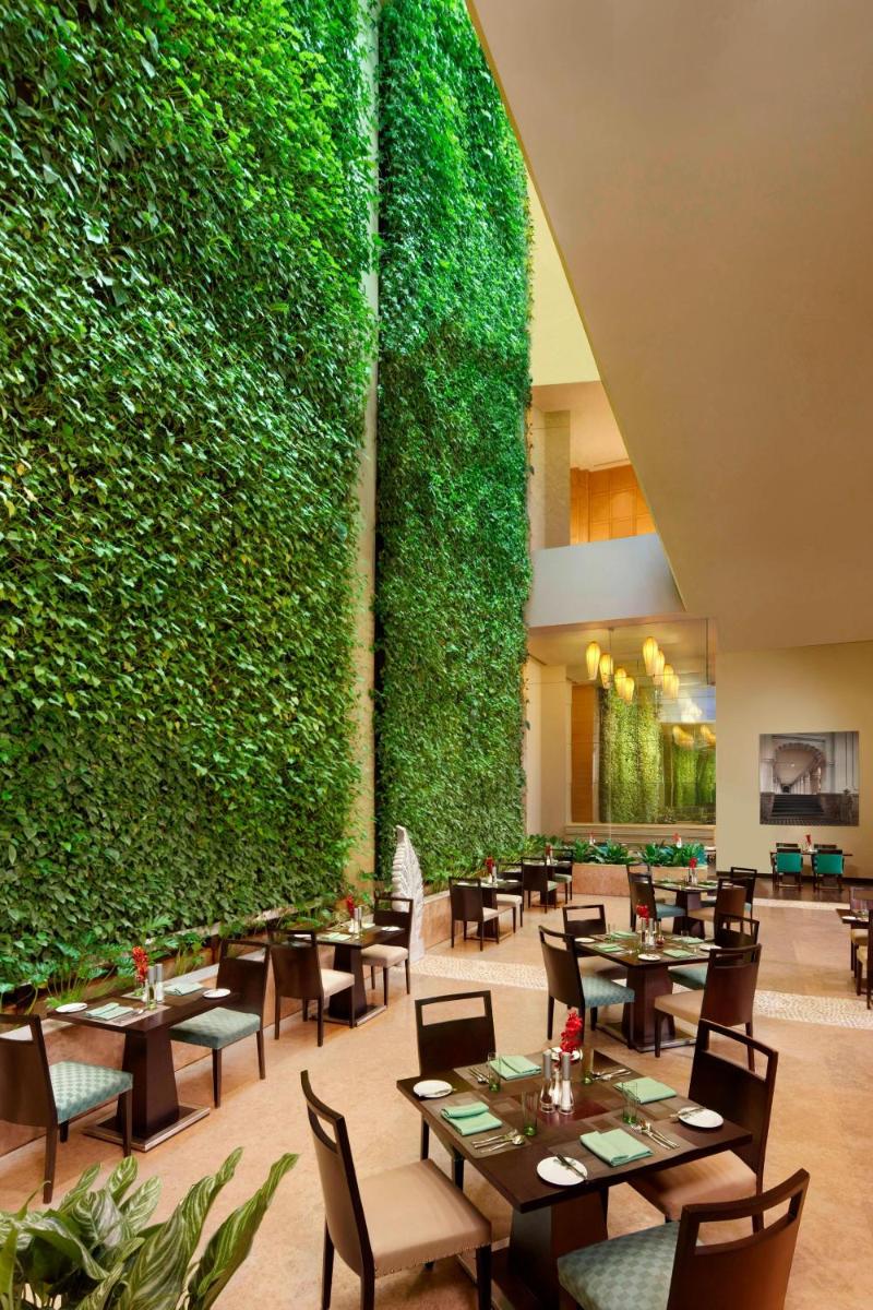 a large green wall in a restaurant with tables and chairs at ITC Gardenia, a Luxury Collection Hotel, Bengaluru in Bengaluru a large green wall in a restaurant with tables and chairs at ITC Gardenia, a Luxury Collection Hotel, Bengaluru in Bengaluru