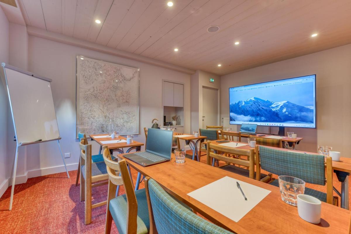 une salle de classe avec des tables et des chaises et un grand écran dans l'établissement Hôtel Lyret, à Chamonix-Mont-Blanc