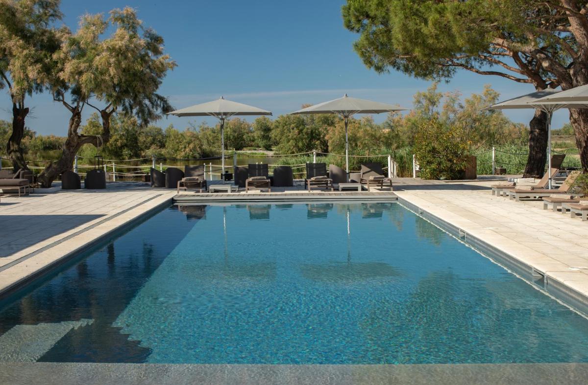 une piscine avec chaises longues et parasols dans l'établissement Mas de la Fouque - Hôtel & Spa, à Saintes-Maries-de-la-Mer