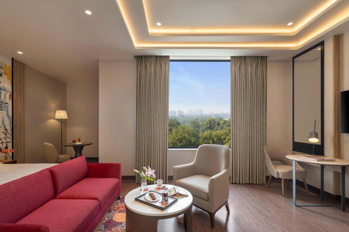 a hotel room with a red couch and a large window at Welcomhotel by ITC Hotels, Delhi-Gurugram Highway in New Delhi a hotel room with a red couch and a large window at Welcomhotel by ITC Hotels, Delhi-Gurugram Highway in New Delhi