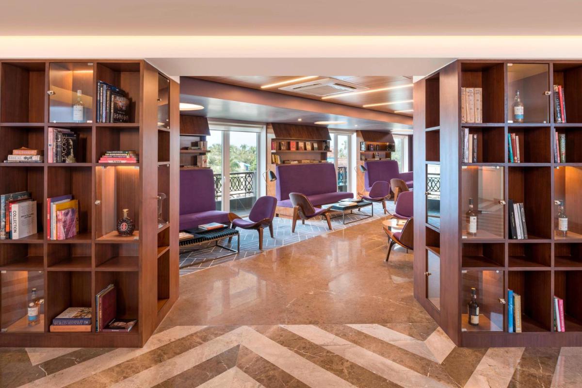 a library with wooden bookshelves and purple chairs at Le Meridien Goa, Calangute in Calangute a library with wooden bookshelves and purple chairs at Le Meridien Goa, Calangute in Calangute