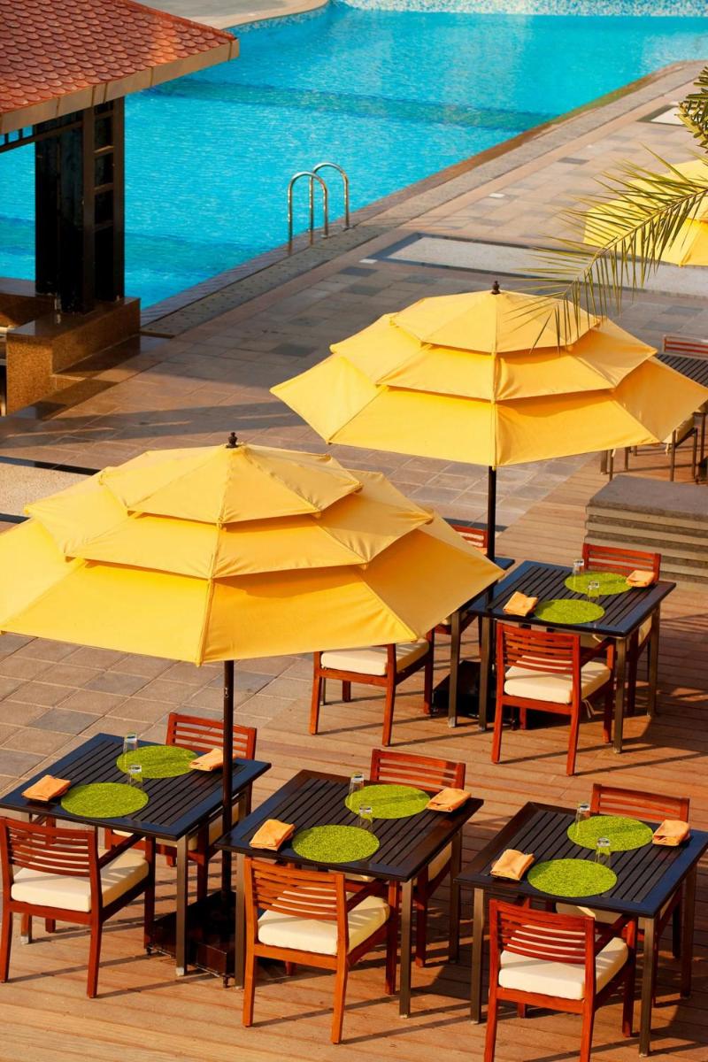 a group of tables with yellow umbrellas next to a pool at The Westin Hyderabad Mindspace in Hyderabad