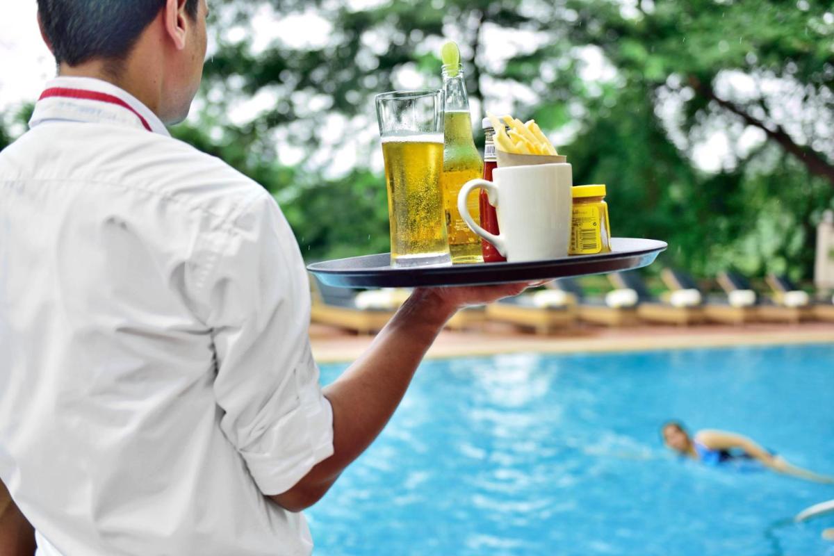 a man holding a tray with drinks and food next to a swimming pool at Marriott Executive Apartment - Lakeside Chalet, Mumbai in Mumbai
