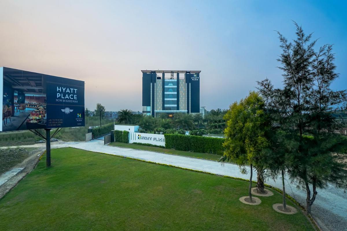 a park with two trees and a large building at Hyatt Place Haridwar in Haridwār
