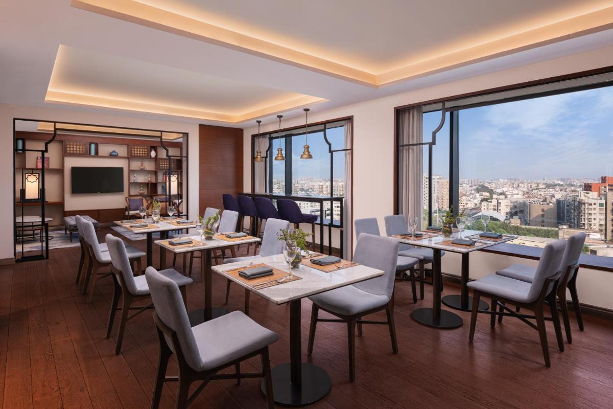 a restaurant with tables and chairs and large windows at Renaissance Ahmedabad Hotel in Ahmedabad