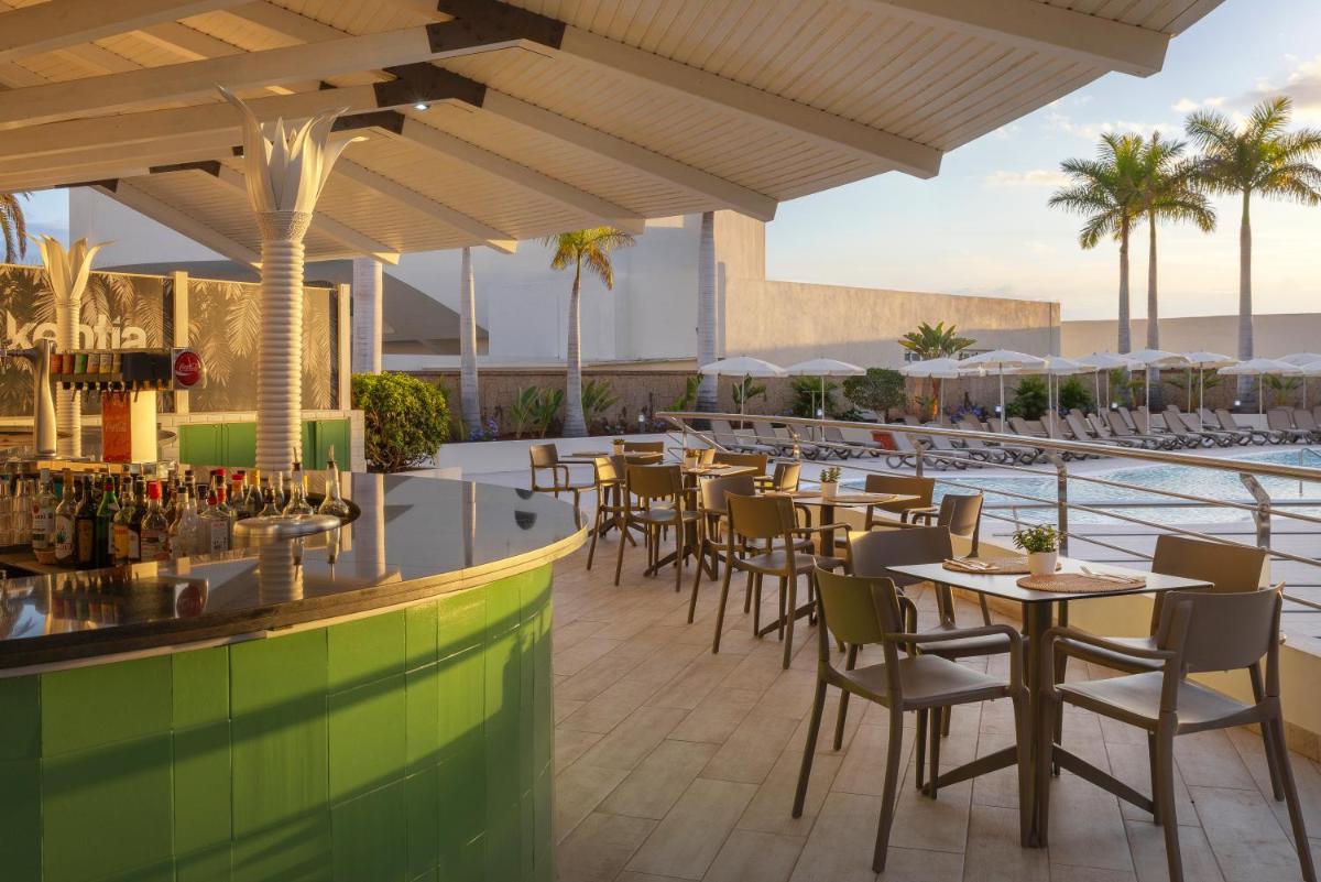 Un restaurante con mesas y sillas junto a una piscina. en AluaSoul Costa Adeje - Adults Only, en Adeje