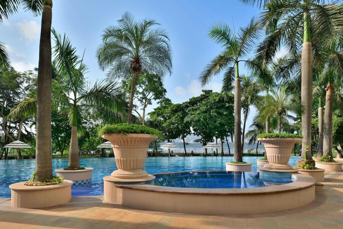 a swimming pool with palm trees and a fountain at The Westin Mumbai Powai Lake in Mumbai