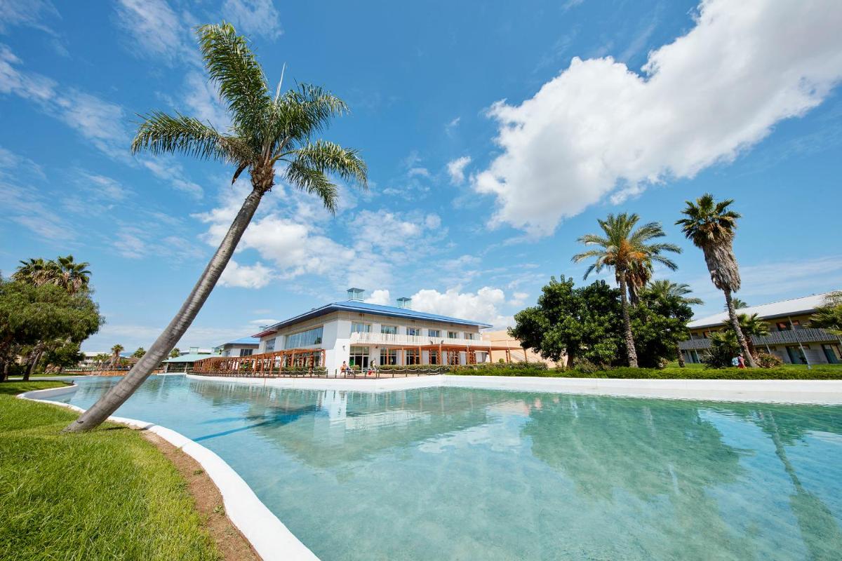 Una piscina con una palmera delante de un edificio. en PortAventura Hotel Caribe - Includes unlimited access to PortAventura Park & 1 access to Ferrari Land, en Salou