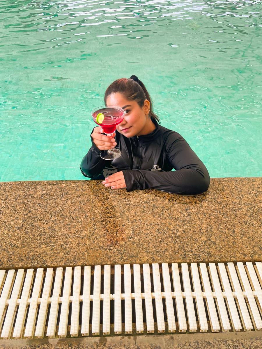 a woman sitting next to a pool holding a drink at Hyatt Place Pune Hinjawadi in Pune