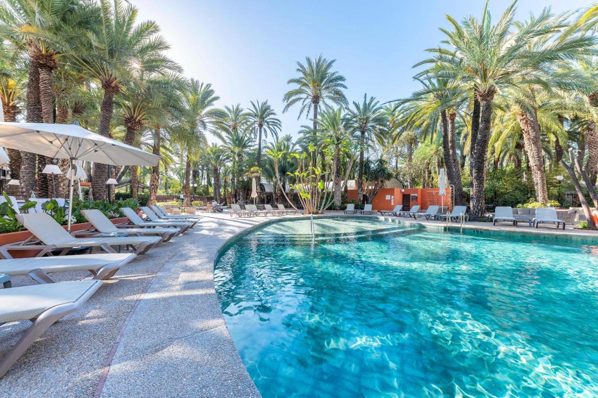 una piscina con tumbonas y palmeras en Hotel Huerto del Cura, en Elche