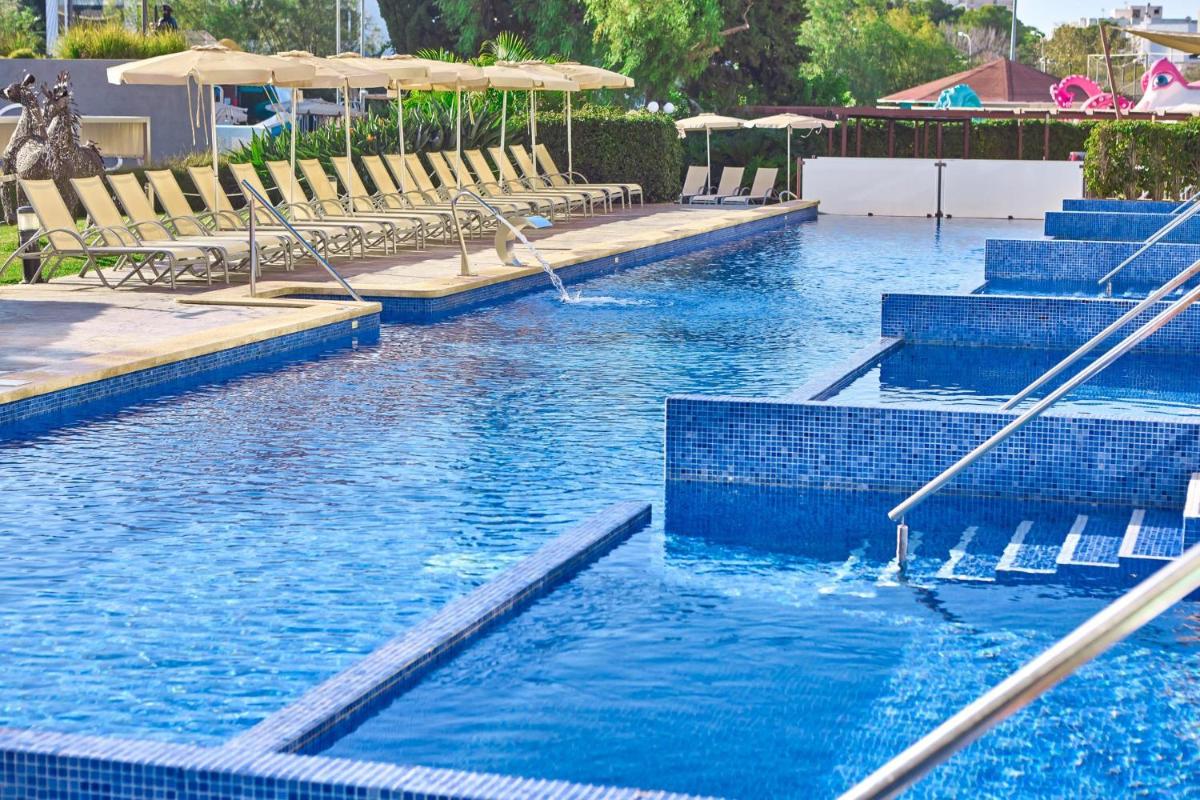 una piscina con agua azul, sillas y sombrillas en Zafiro Palmanova, en Palmanova