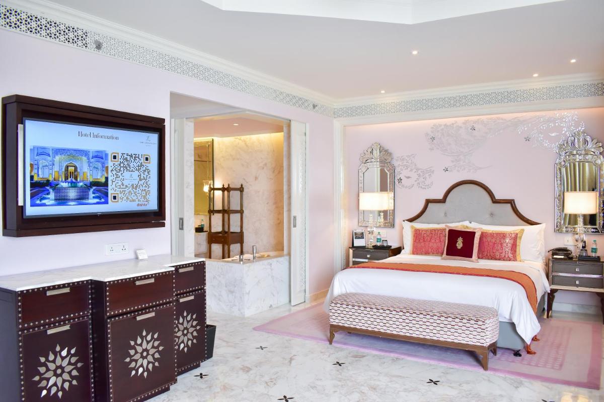 a bedroom with a bed and a tv on a wall at The Leela Palace Jaipur in Jaipur