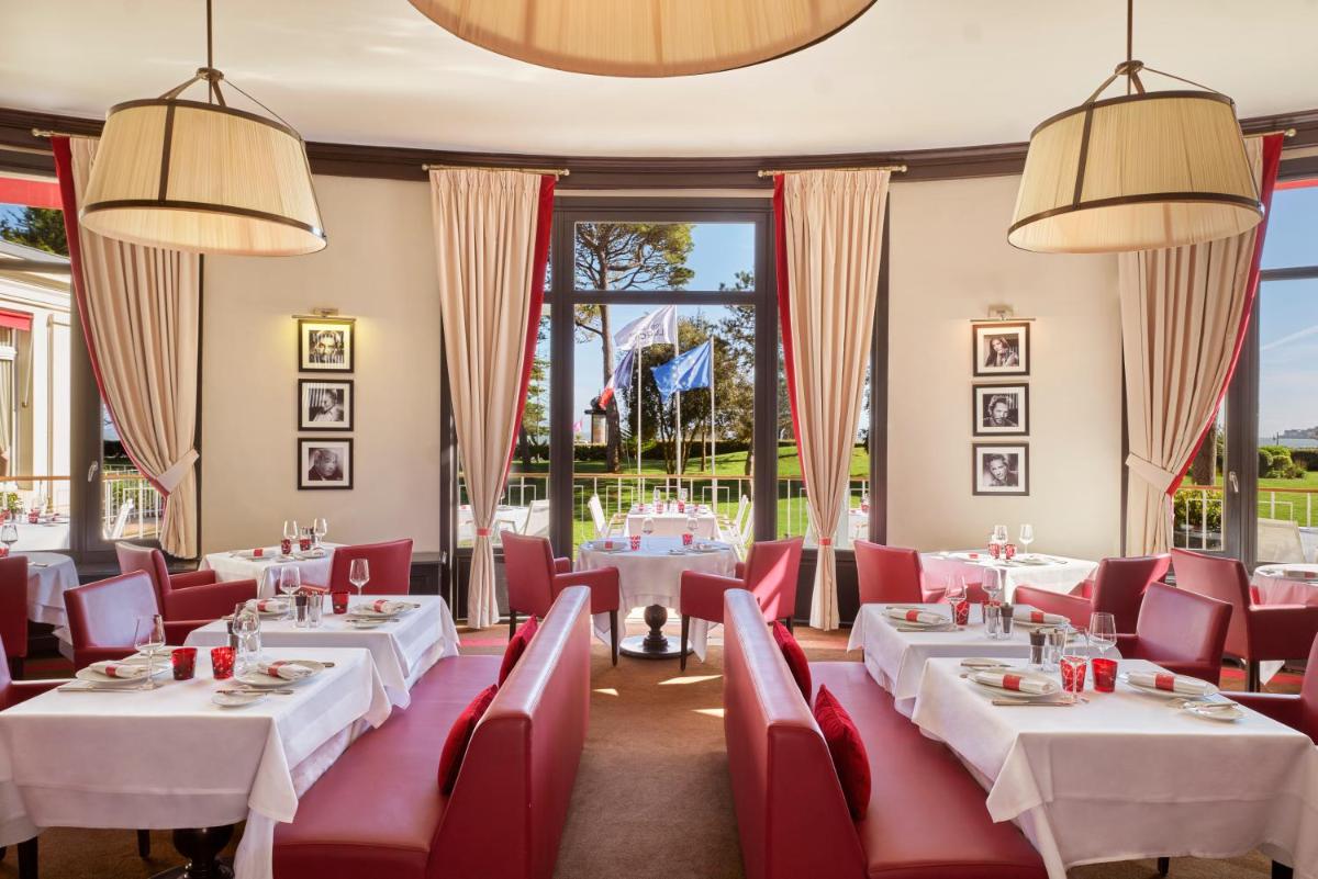 un restaurant avec des tables blanches et des chaises rouges dans l'établissement Hôtel Barrière Le Royal La Baule, à La Baule