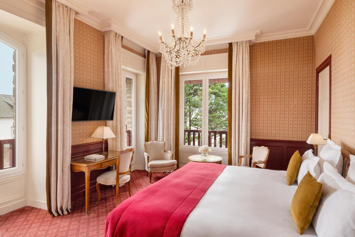 une chambre avec un grand lit et un lustre dans l'établissement Le Castel Marie Louise, à La Baule