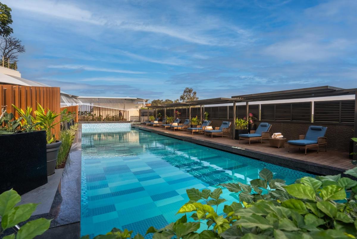 a swimming pool with chairs and tables next to a building at Hyatt Centric MG Road Bangalore in Bengaluru a swimming pool with chairs and tables next to a building at Hyatt Centric MG Road Bangalore in Bengaluru