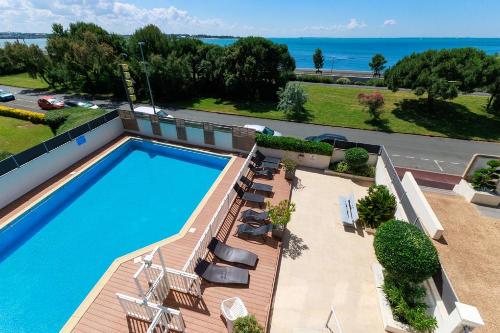 une vue aérienne d'une piscine avec des chaises et de l'océan dans l'établissement Logis Hôtel Le Rochelois, à La Rochelle