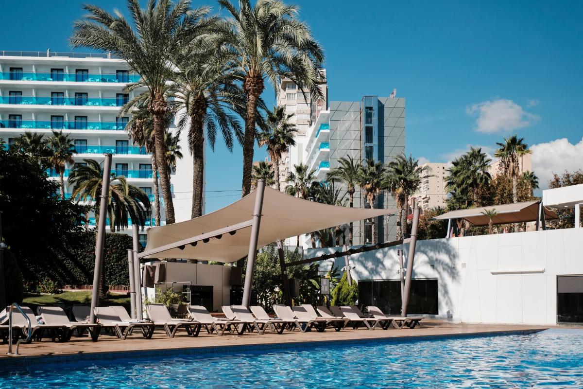 una piscina con sillas y palmeras y un edificio en Helios Benidorm, en Benidorm