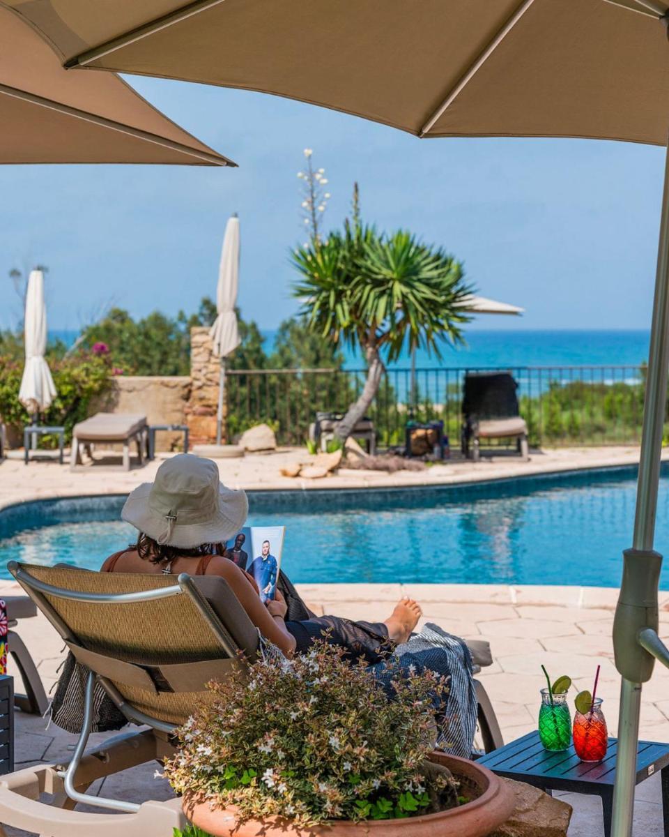 une femme assise sur une chaise en train de lire un livre au bord d'une piscine dans l'établissement La Solenzara hôtel - 3 Etoiles Supérieur - Appartement & SPA, à Sari-Solenzara