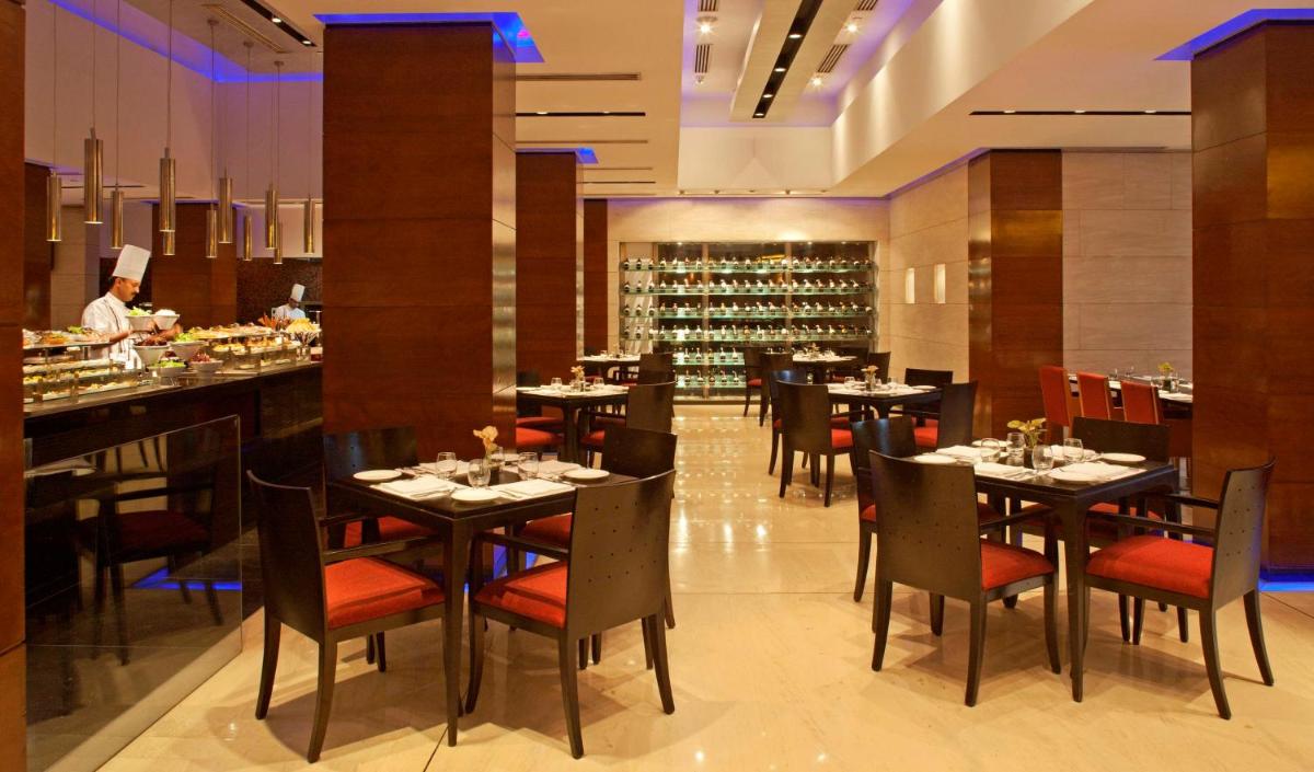a restaurant with tables and chairs and a chef in the background at Radisson Blu Plaza Delhi Airport in New Delhi a restaurant with tables and chairs and a chef in the background at Radisson Blu Plaza Delhi Airport in New Delhi