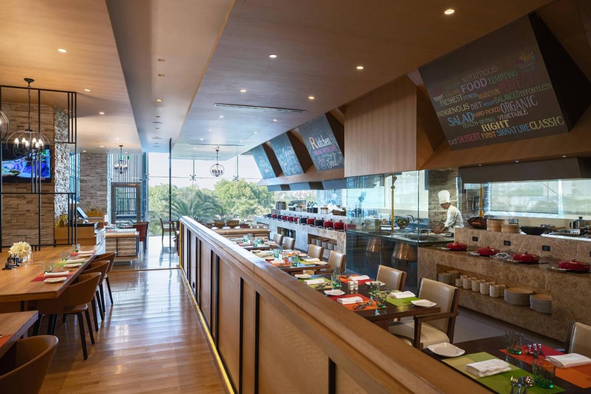 a restaurant with a long counter with tables and chairs at Renaissance Ahmedabad Hotel in Ahmedabad