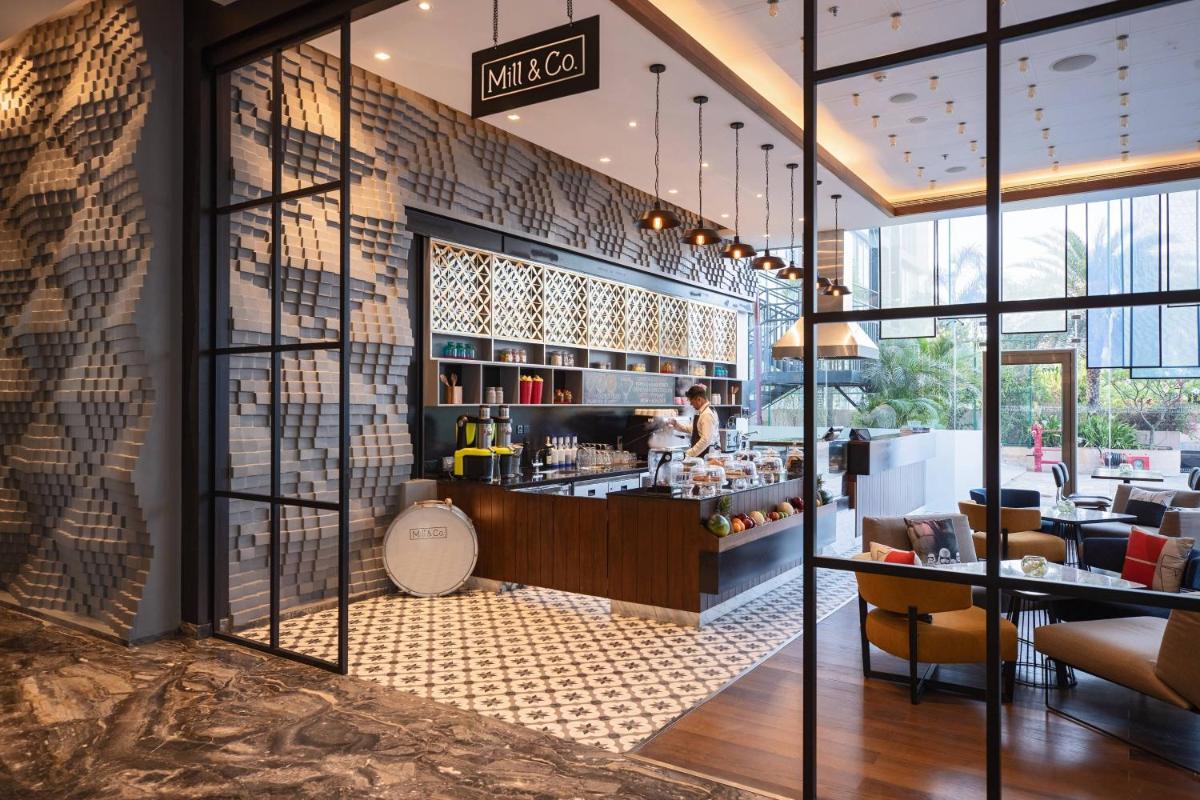 a lobby of a restaurant with a woman behind a counter at Renaissance Ahmedabad Hotel in Ahmedabad