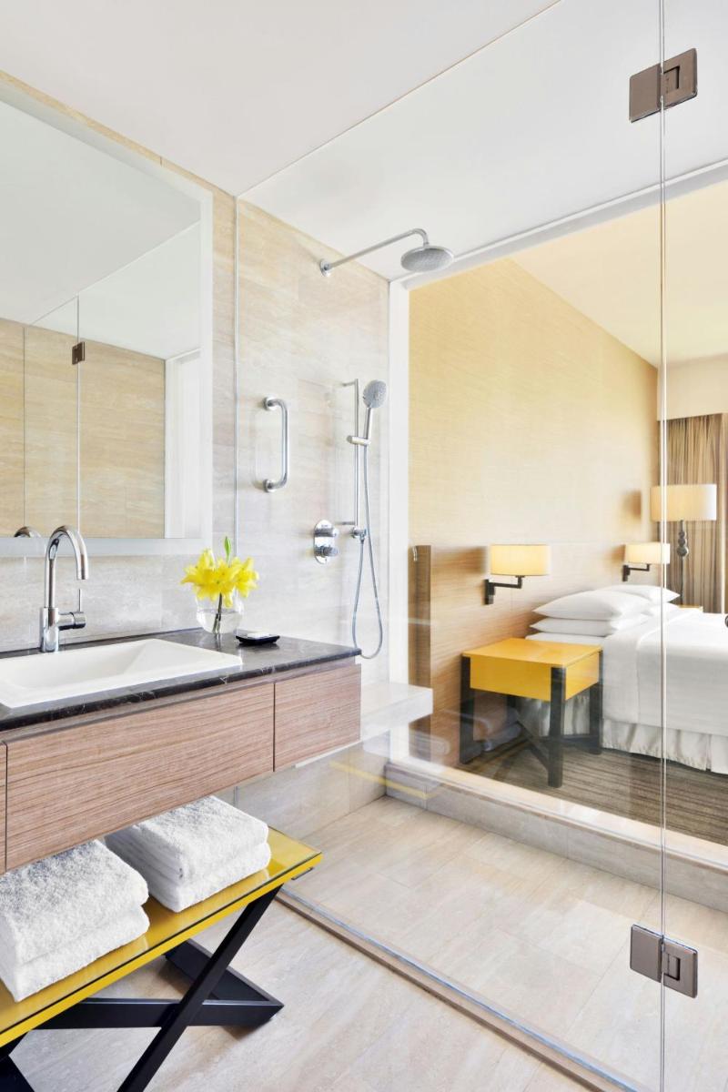 a bathroom with a shower and a sink and a bed at Courtyard by Marriott Bengaluru Outer Ring Road in Bengaluru
