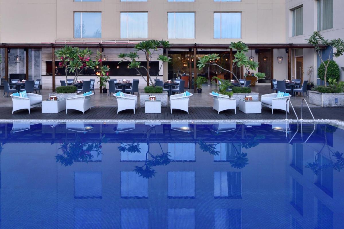 a hotel with tables and chairs next to a pool at Courtyard by Marriott Bengaluru Outer Ring Road in Bengaluru a hotel with tables and chairs next to a pool at Courtyard by Marriott Bengaluru Outer Ring Road in Bengaluru