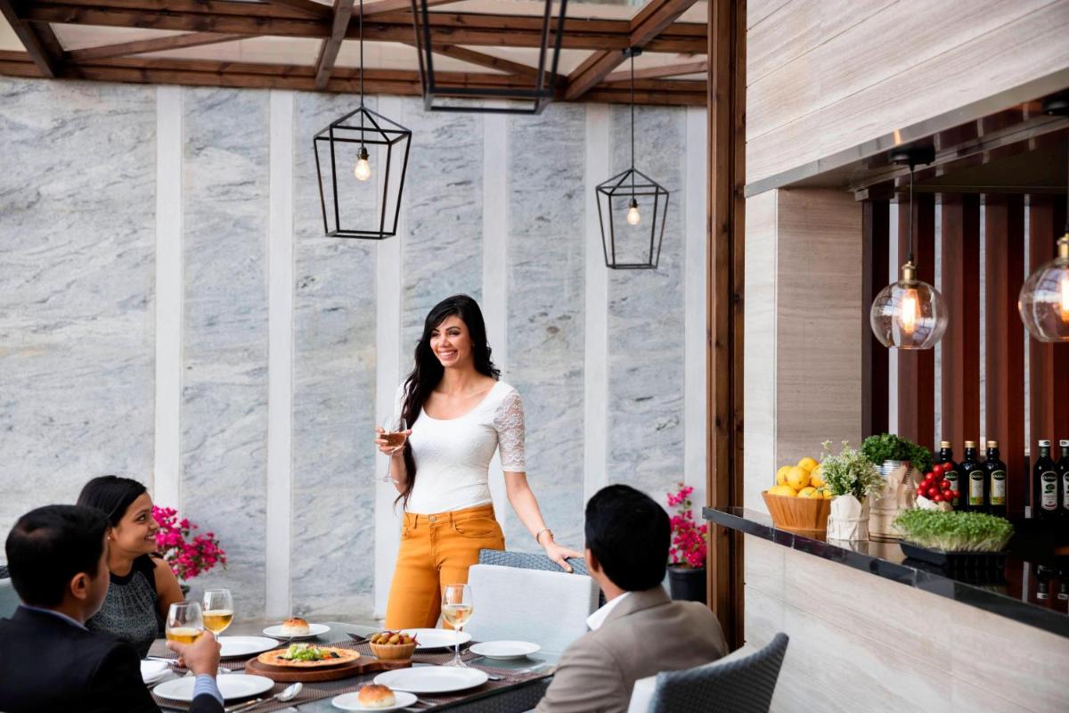 a woman standing at a table in a restaurant at Courtyard by Marriott Bengaluru Outer Ring Road in Bengaluru