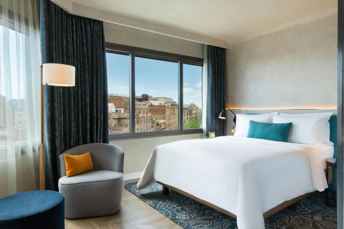 1 dormitorio con cama, silla y ventana grande en Renaissance Barcelona Hotel, en Barcelona