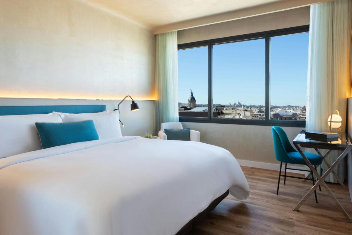 Un dormitorio con una cama y un escritorio y una gran ventana. en Renaissance Barcelona Hotel, en Barcelona