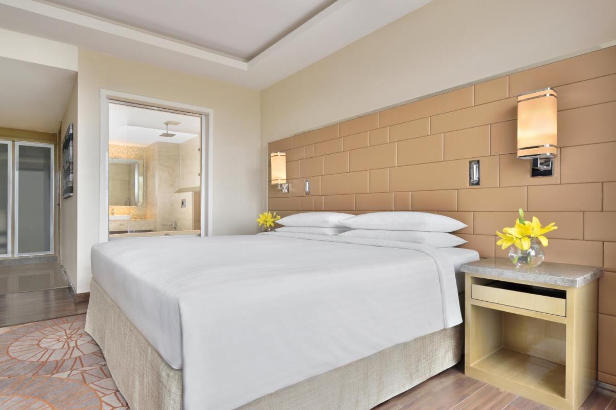 a bedroom with a large white bed and a bathroom at Courtyard by Marriott Bengaluru Hebbal in Bengaluru
