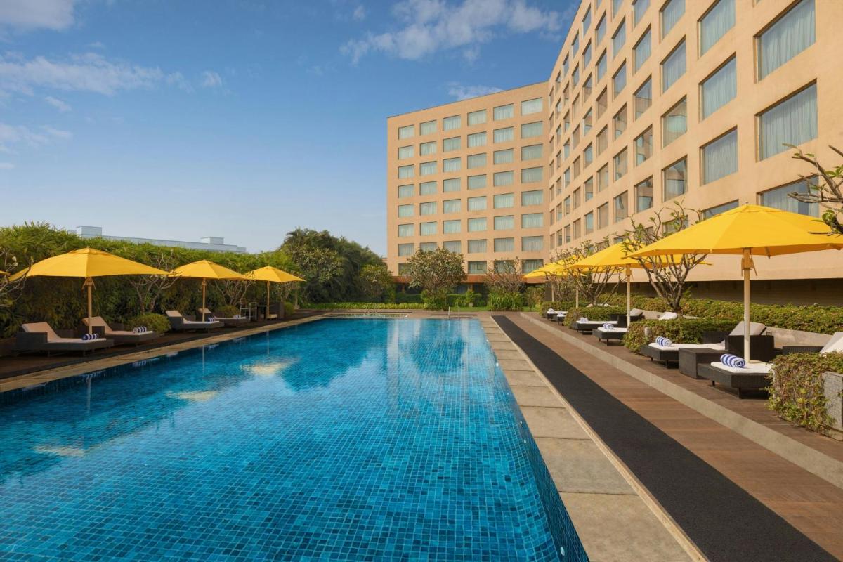 a swimming pool with umbrellas and chairs and a building at Courtyard by Marriott Mumbai International Airport in Mumbai a swimming pool with umbrellas and chairs and a building at Courtyard by Marriott Mumbai International Airport in Mumbai