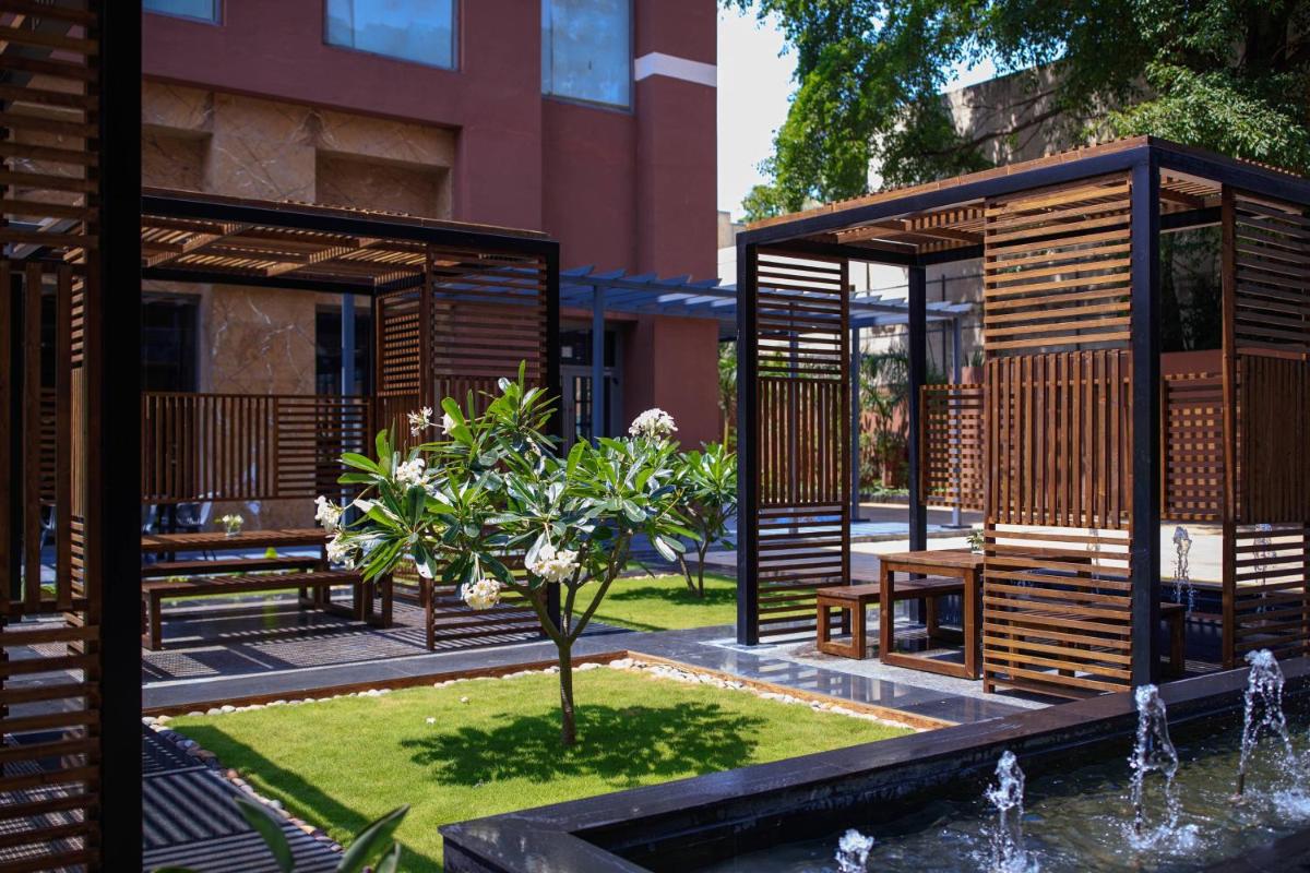 a garden with wooden benches and a tree and a fountain at Renaissance Bengaluru Race Course Hotel in Bengaluru