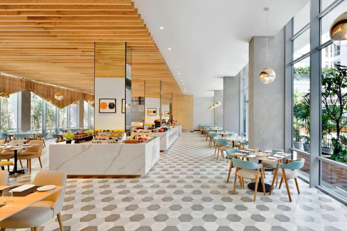 a restaurant with tables and chairs and windows at Aloft New Delhi Aerocity in New Delhi a restaurant with tables and chairs and windows at Aloft New Delhi Aerocity in New Delhi