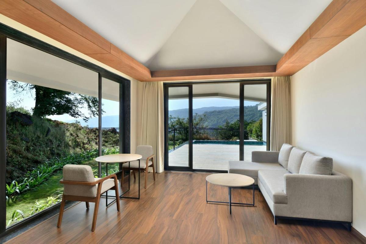 a living room with a couch and tables and large windows at Courtyard by Marriott Mahabaleshwar in Mahabaleshwar