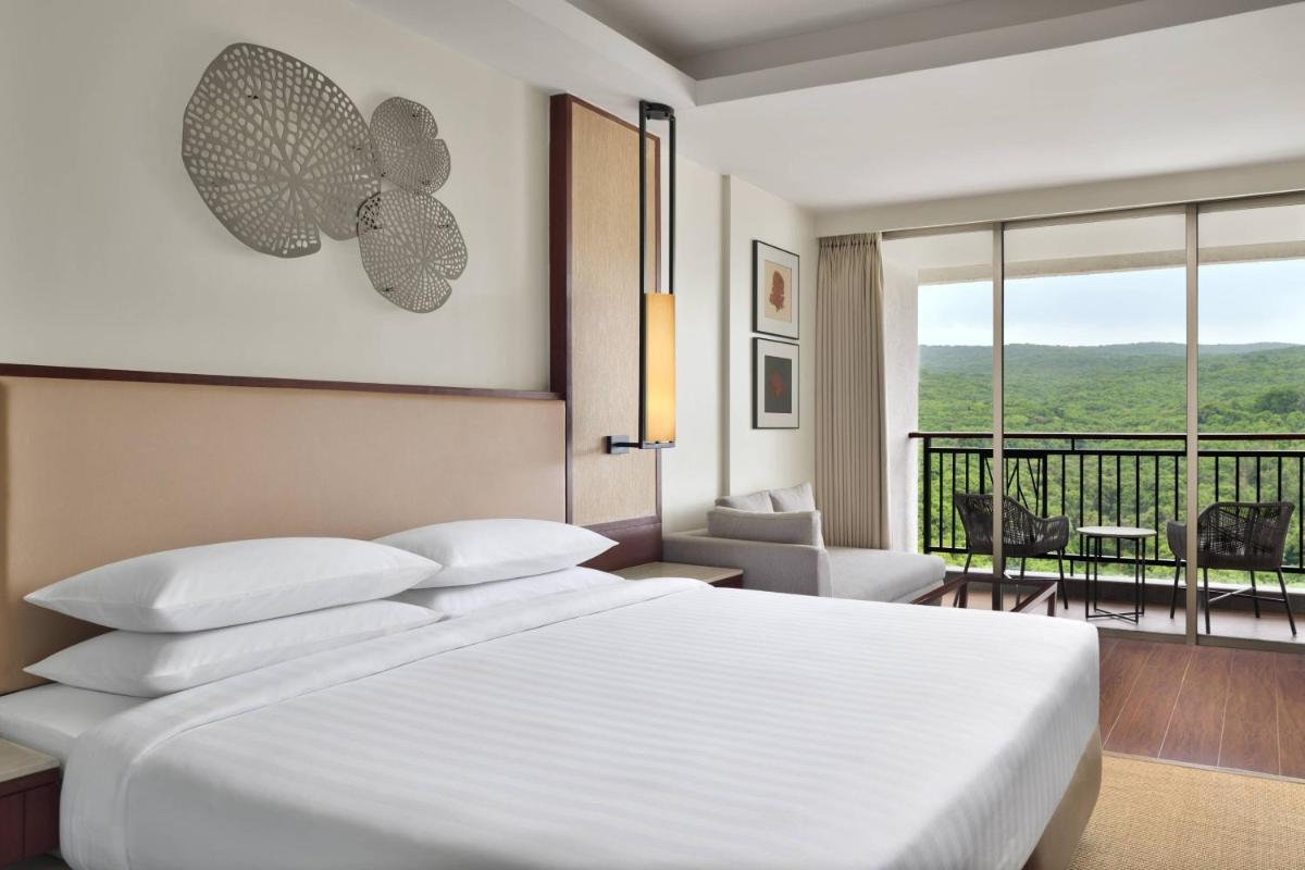 a bedroom with a white bed and a balcony at Courtyard by Marriott Mahabaleshwar in Mahabaleshwar