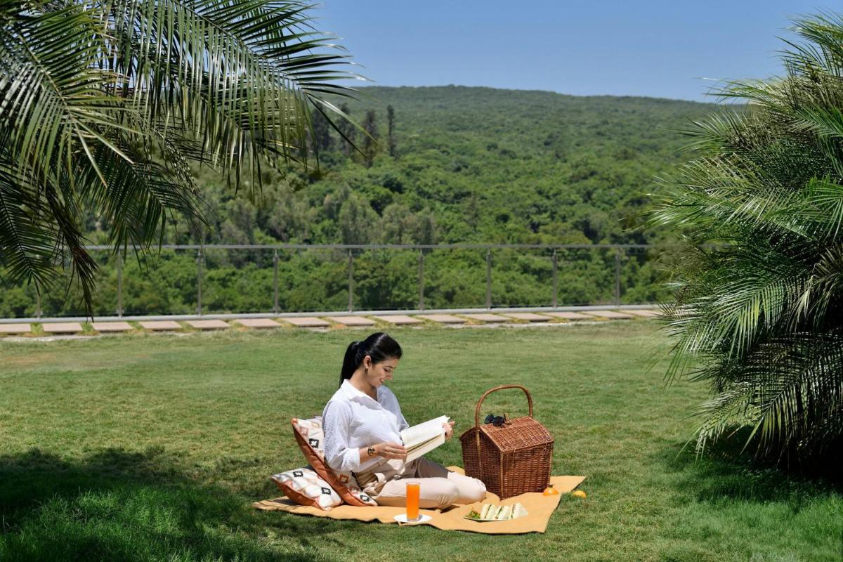 a woman sitting on a blanket reading a book at Courtyard by Marriott Mahabaleshwar in Mahabaleshwar
