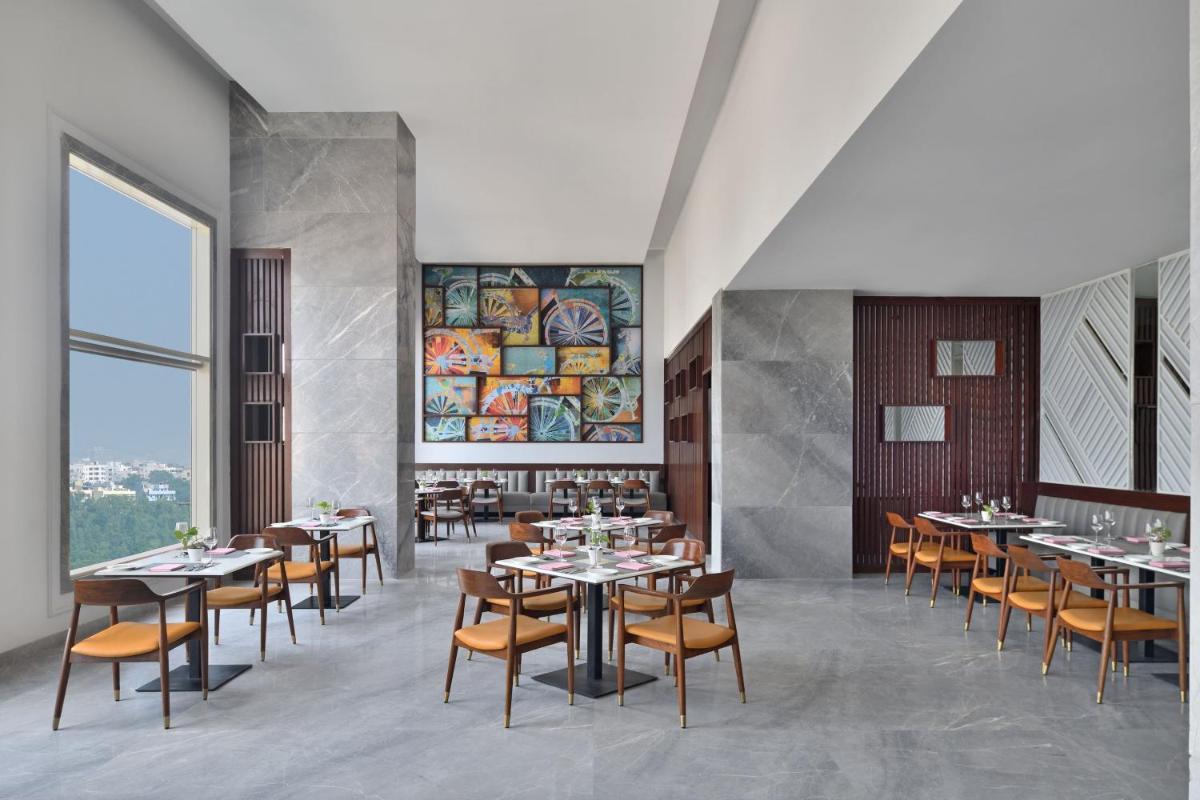 a restaurant with tables and chairs and a large window at Le Meridien Hyderabad in Hyderabad