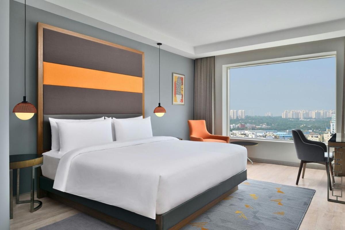 a bedroom with a large white bed and a large window at Le Meridien Hyderabad in Hyderabad