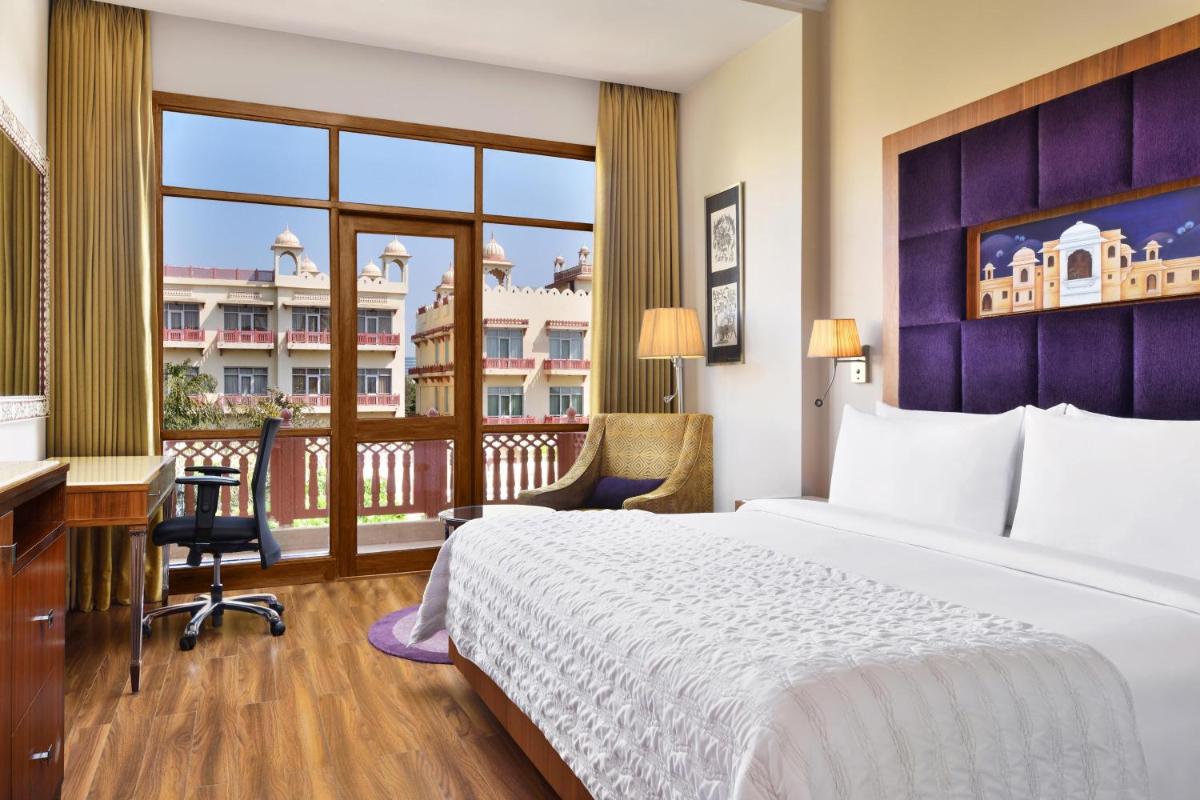 a hotel room with a bed and a desk and a balcony at Le Meridien Jaipur Resort & Spa in Jaipur