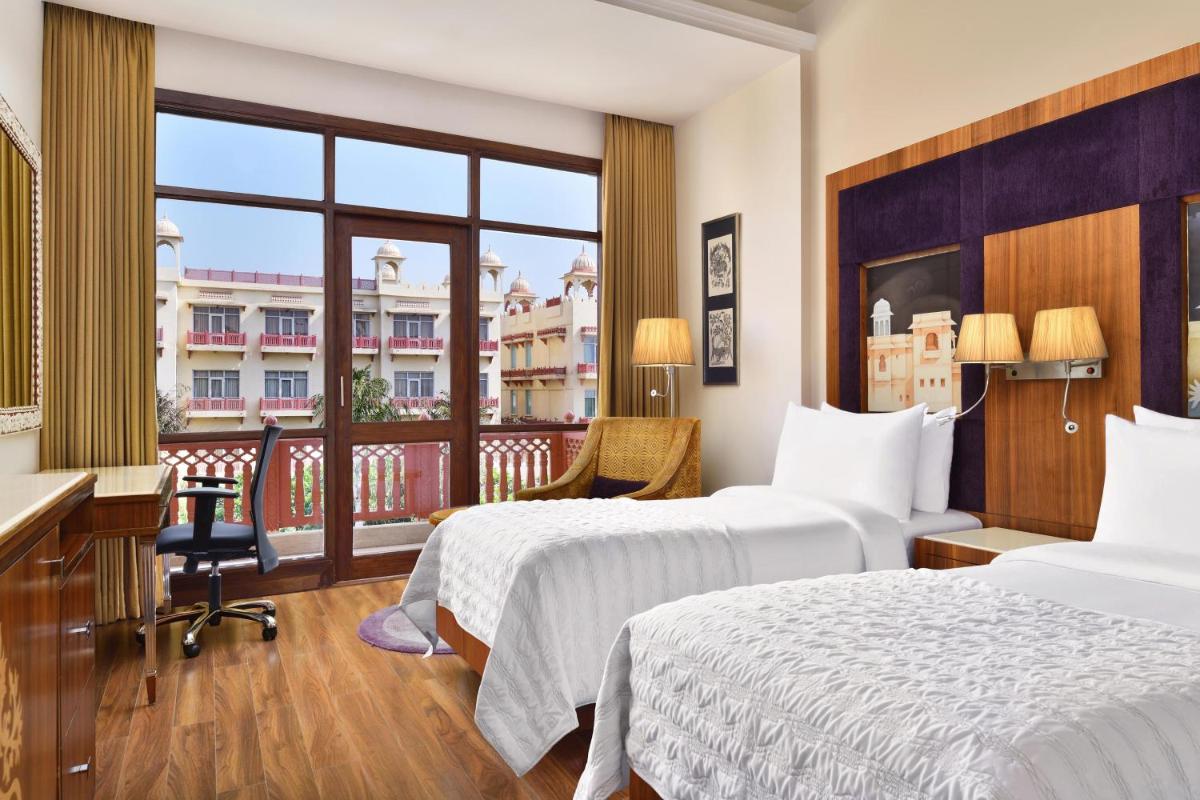 a hotel room with two beds and a balcony at Le Meridien Jaipur Resort & Spa in Jaipur