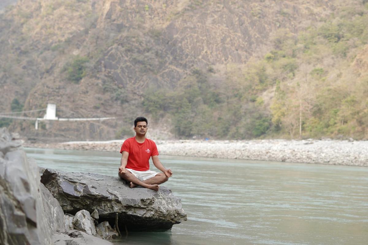 a man sitting on a rock in the middle of a river at Raga on the Ganges, Rishikesh in Rishīkesh